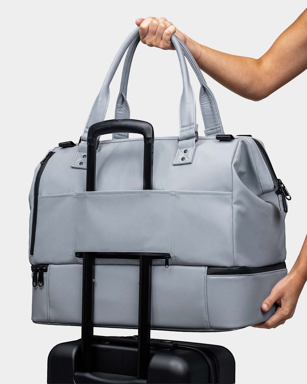 Gray travel bag with wheels held by a person against a light gray background