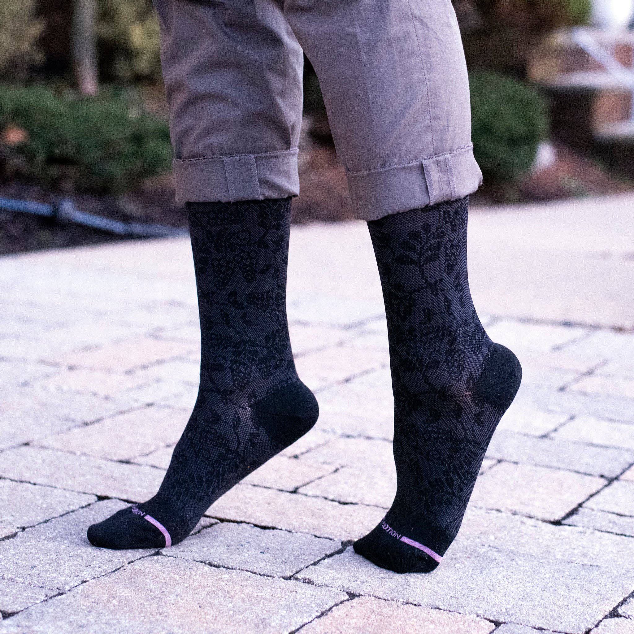 Person wearing black patterned socks on a paved walkway with a garden background