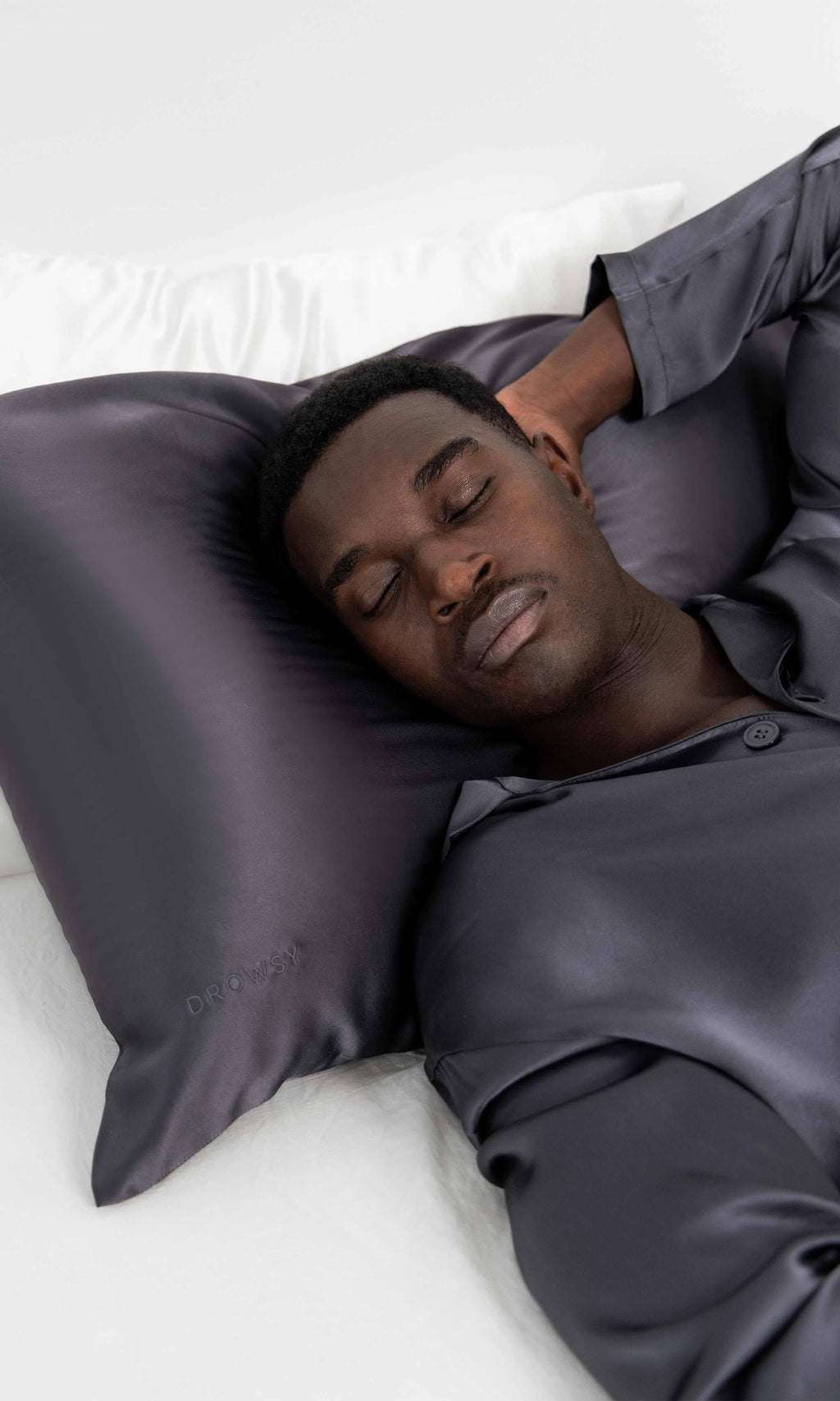 Man lying on a bed with a grey silk pillow.