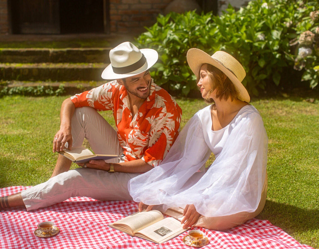 Two people sitting on a picnic blanket in a garden, reading books.