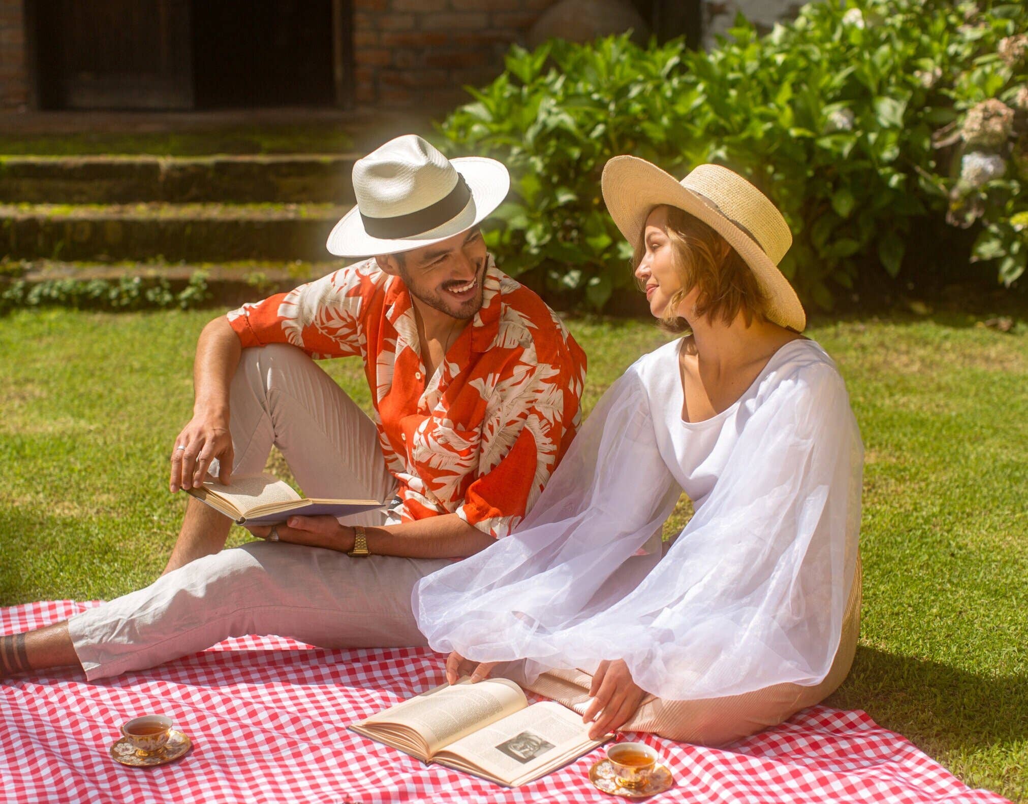 Two people sitting on a picnic blanket in a garden, reading books.