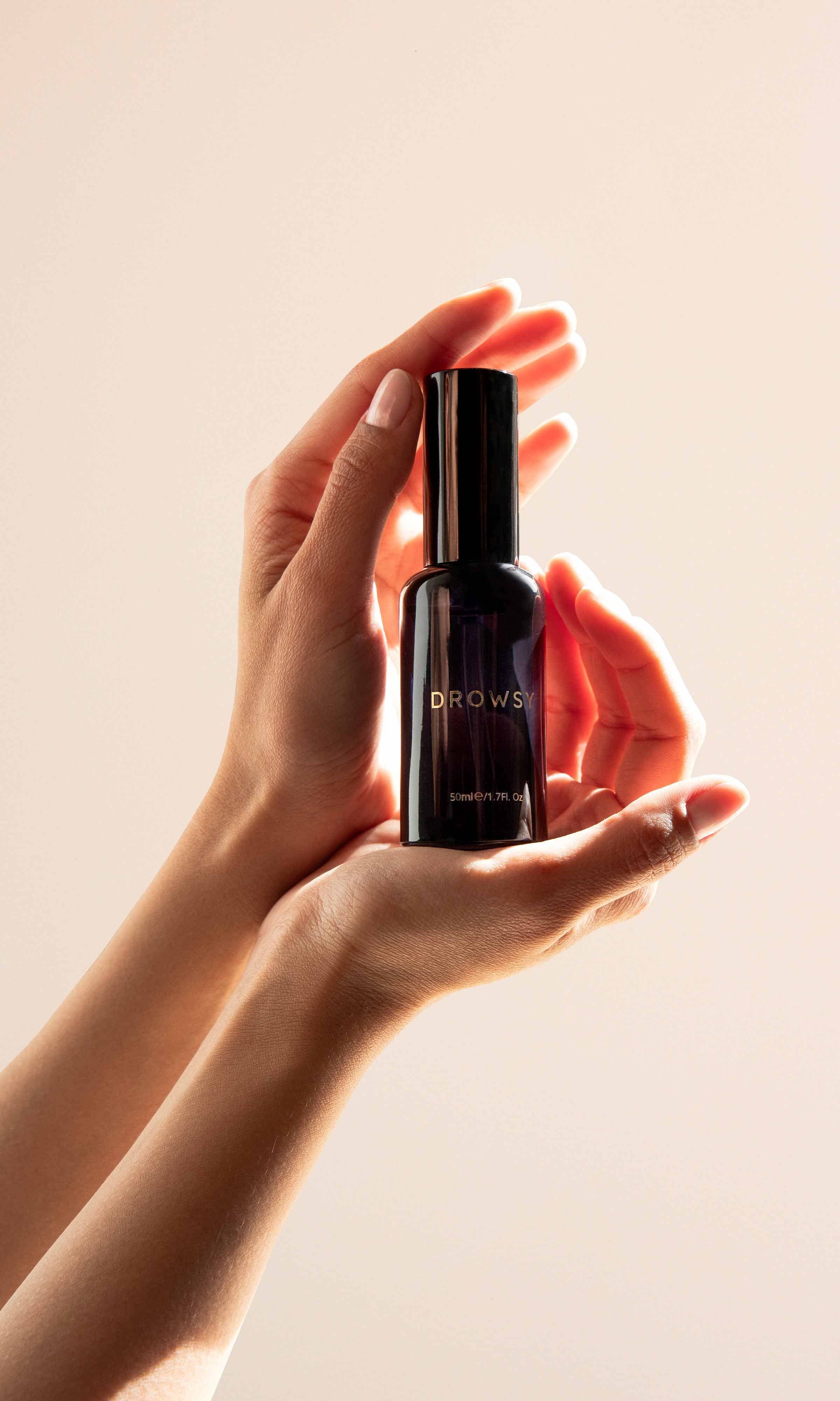 Hand holding a black bottle labeled Drowsy against a beige background
