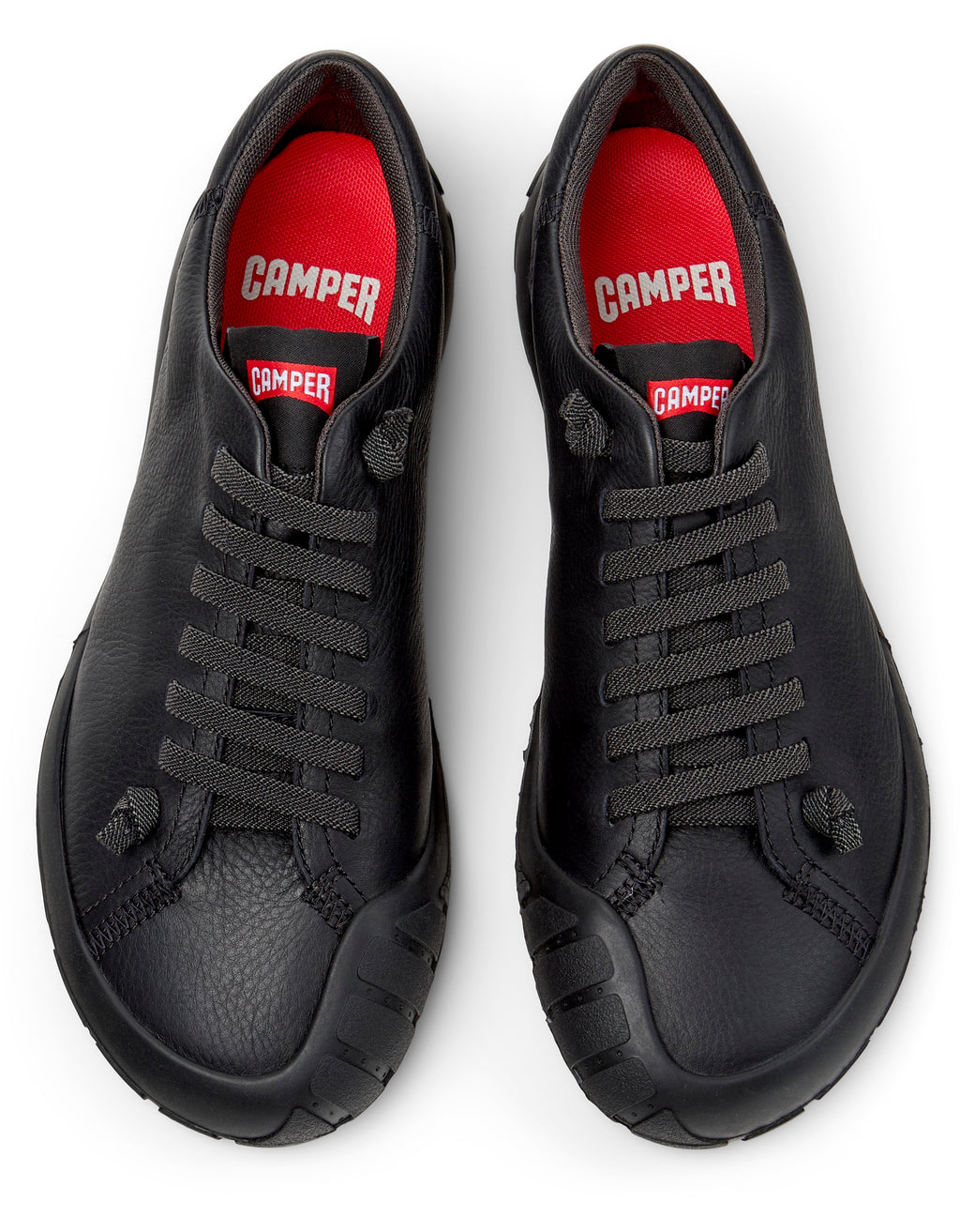 Black sneakers with red interior and 'Camper' branding on a white background