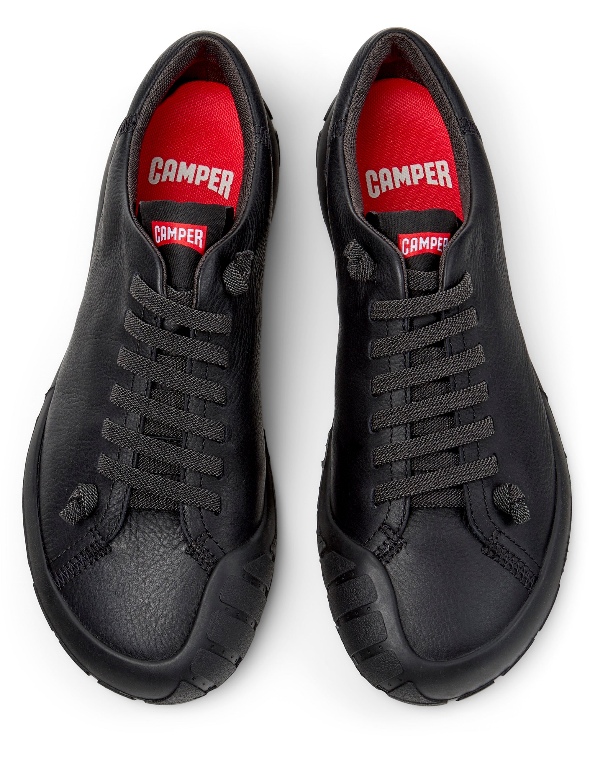 Black sneakers with red interior and 'Camper' branding on a white background