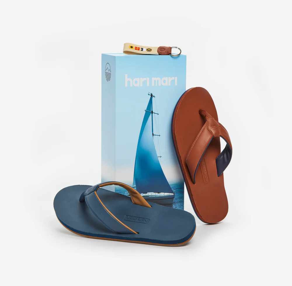 Pair of blue and brown flip-flops with a Harimari box featuring a sailboat design on a light gray background.