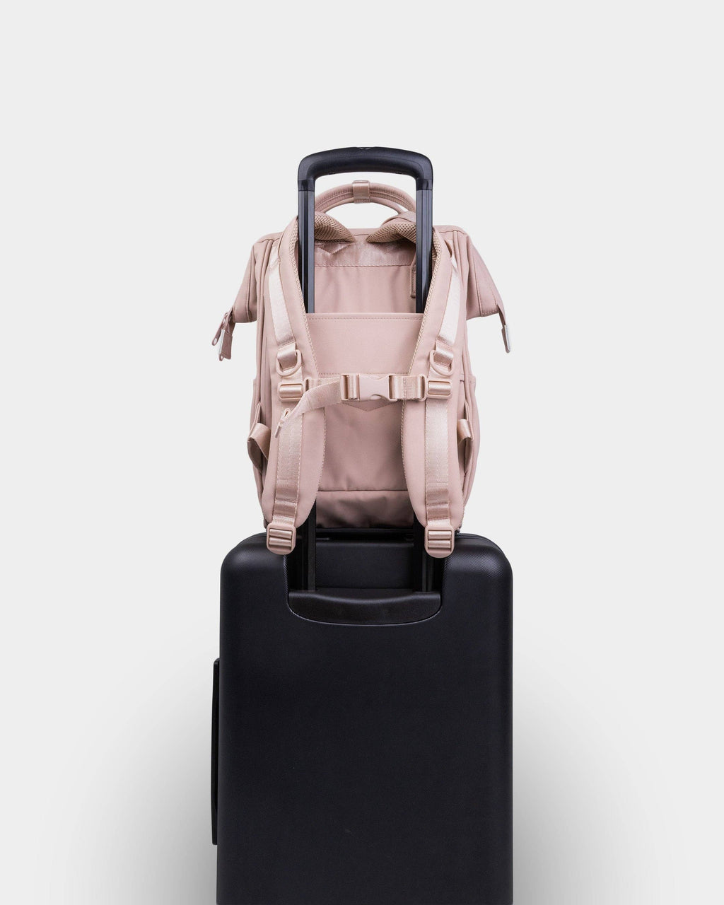 Beige backpack on a black suitcase against a white background