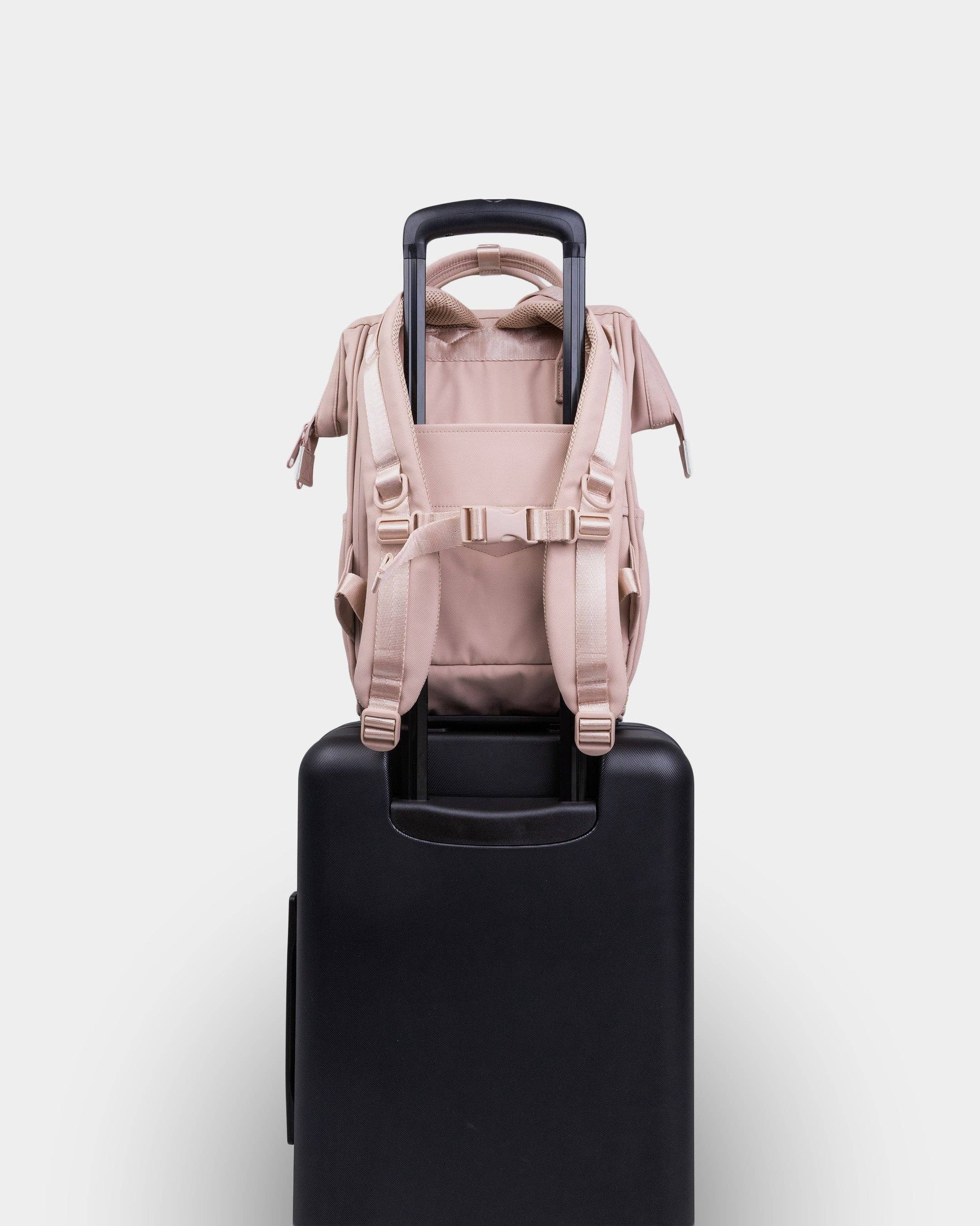 Beige backpack on a black suitcase against a white background