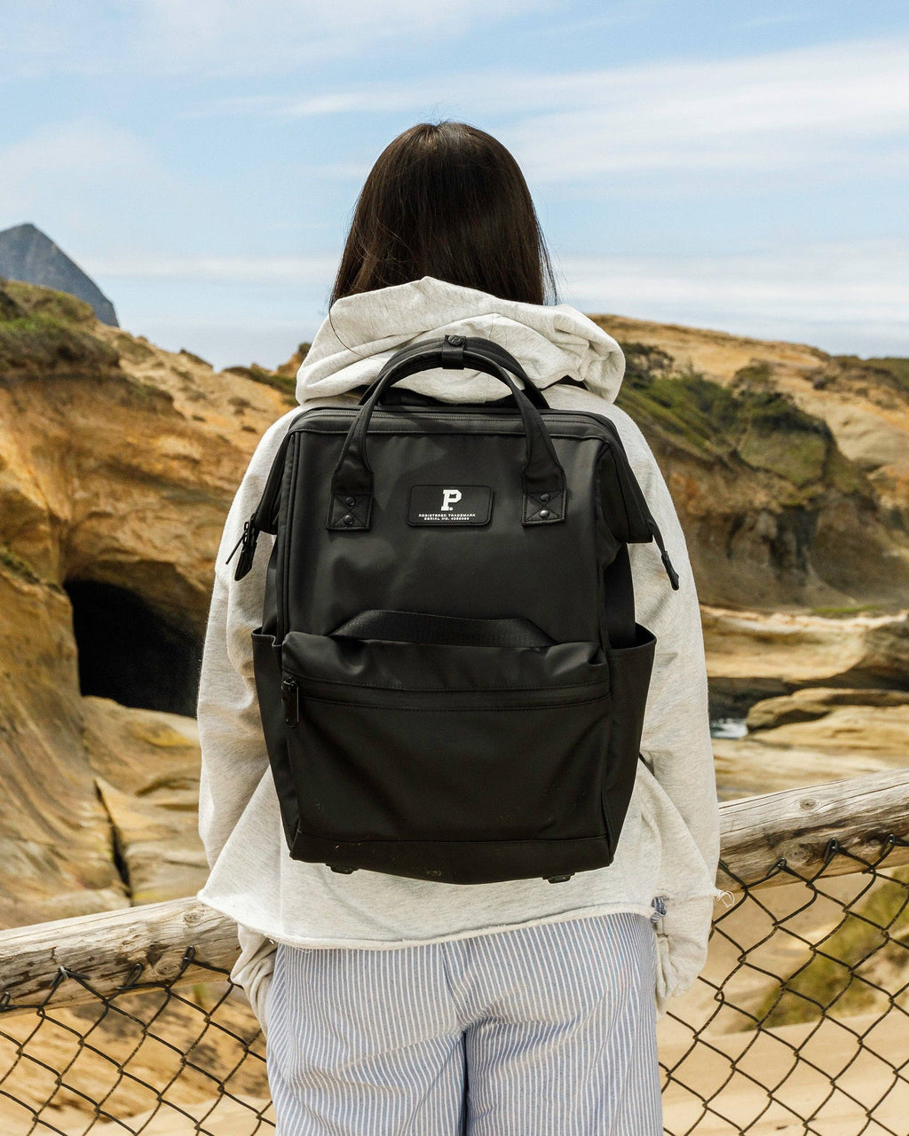 Person wearing a black backpack with a logo, standing on a rocky landscape.