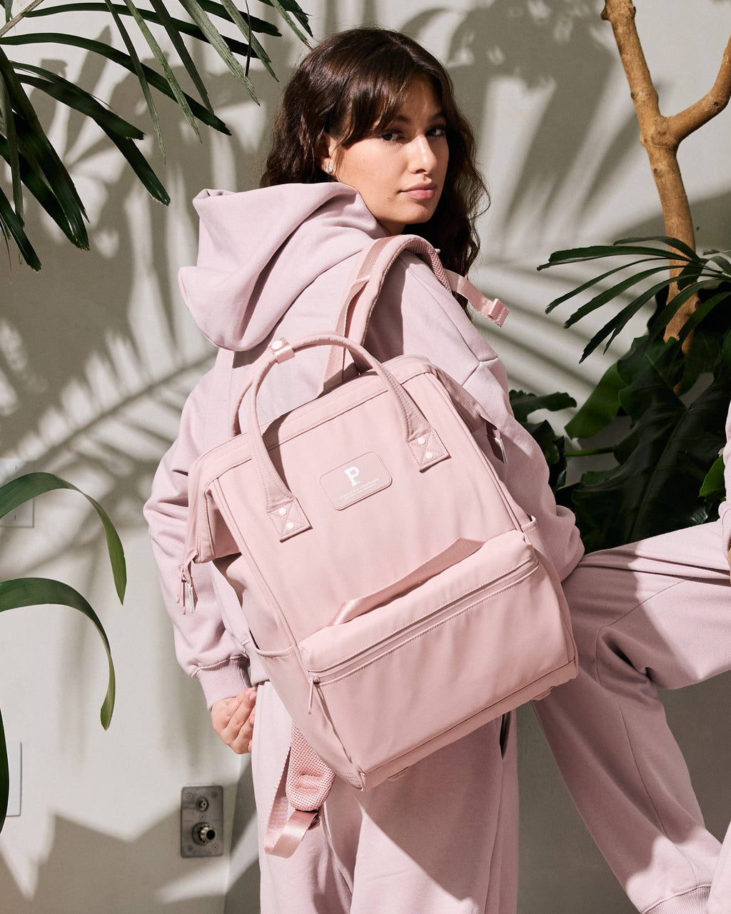 Person wearing a pink outfit with a matching backpack in a plant-filled room