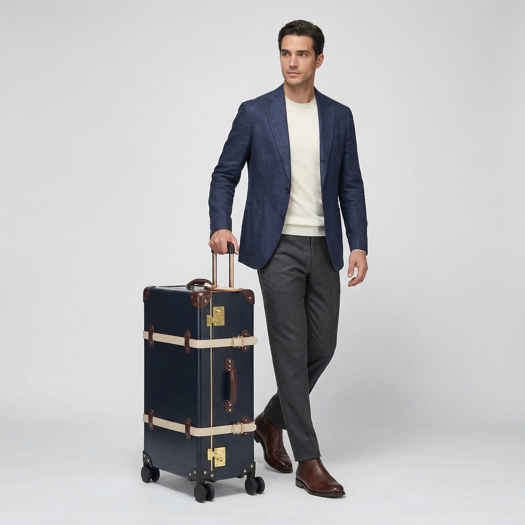 Man in a suit standing next to a vintage-style suitcase on a plain background