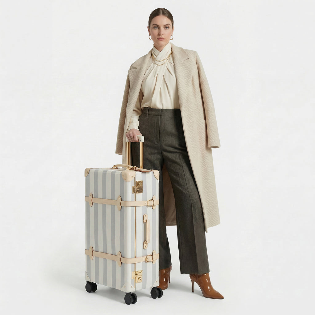 Woman holding a striped suitcase wearing a beige coat and brown pants on a white background