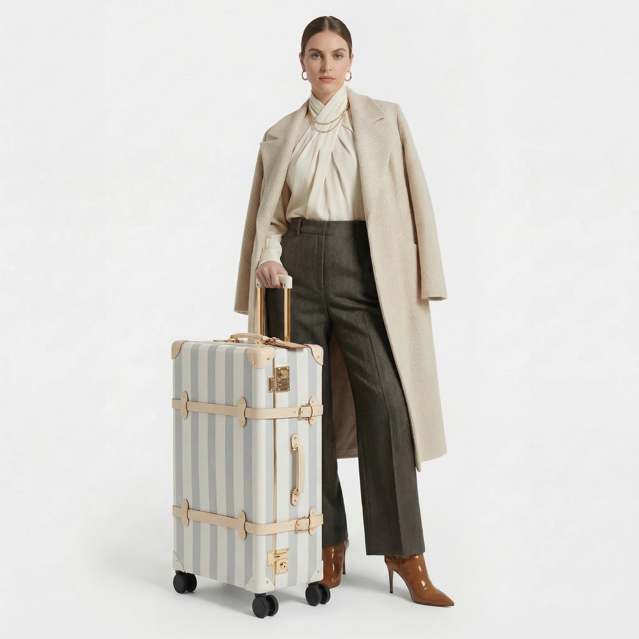 Woman holding a striped suitcase wearing a beige coat and brown pants on a white background
