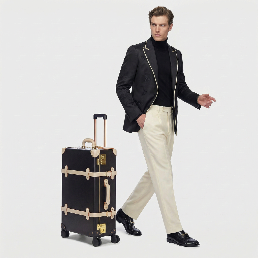 Man in formal attire standing next to a black suitcase with beige straps on a white background