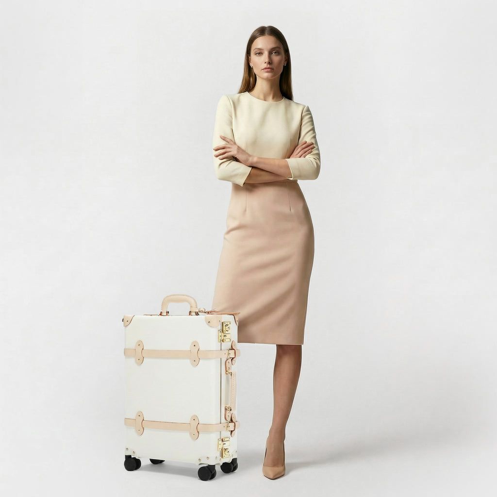 Woman in a beige outfit standing next to a white suitcase on a light gray background