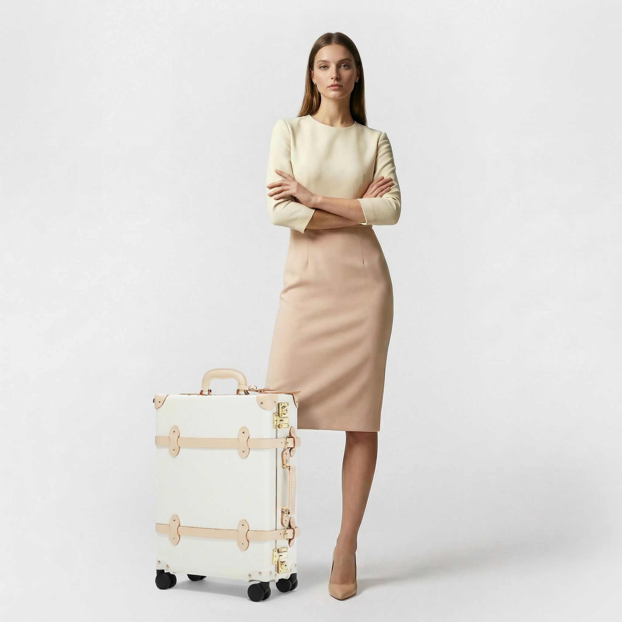 Woman in a beige outfit standing next to a white suitcase on a light gray background