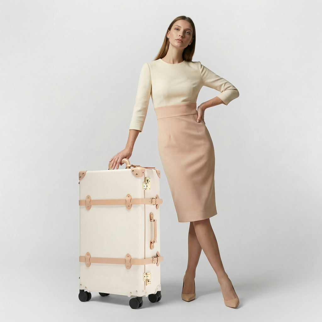Woman holding a cream suitcase against a plain background