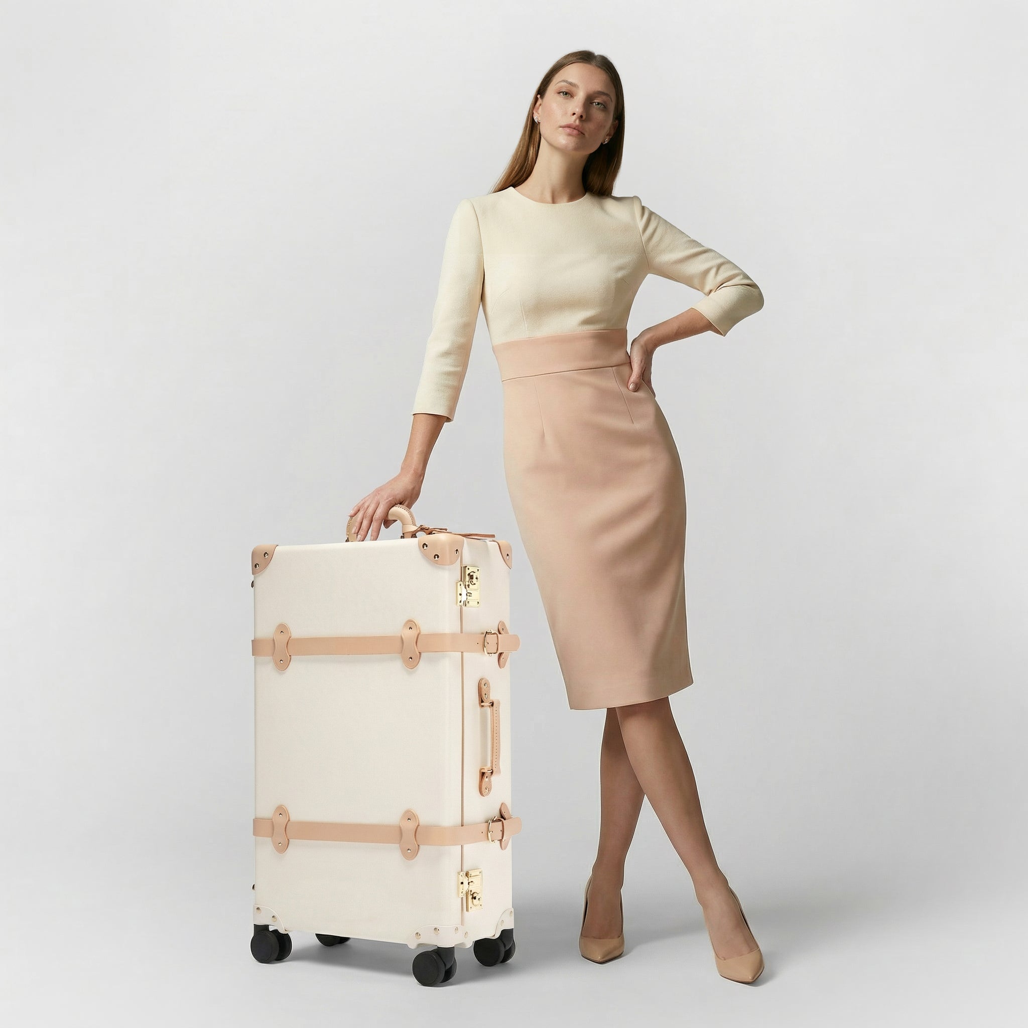 Woman holding a cream suitcase against a plain background