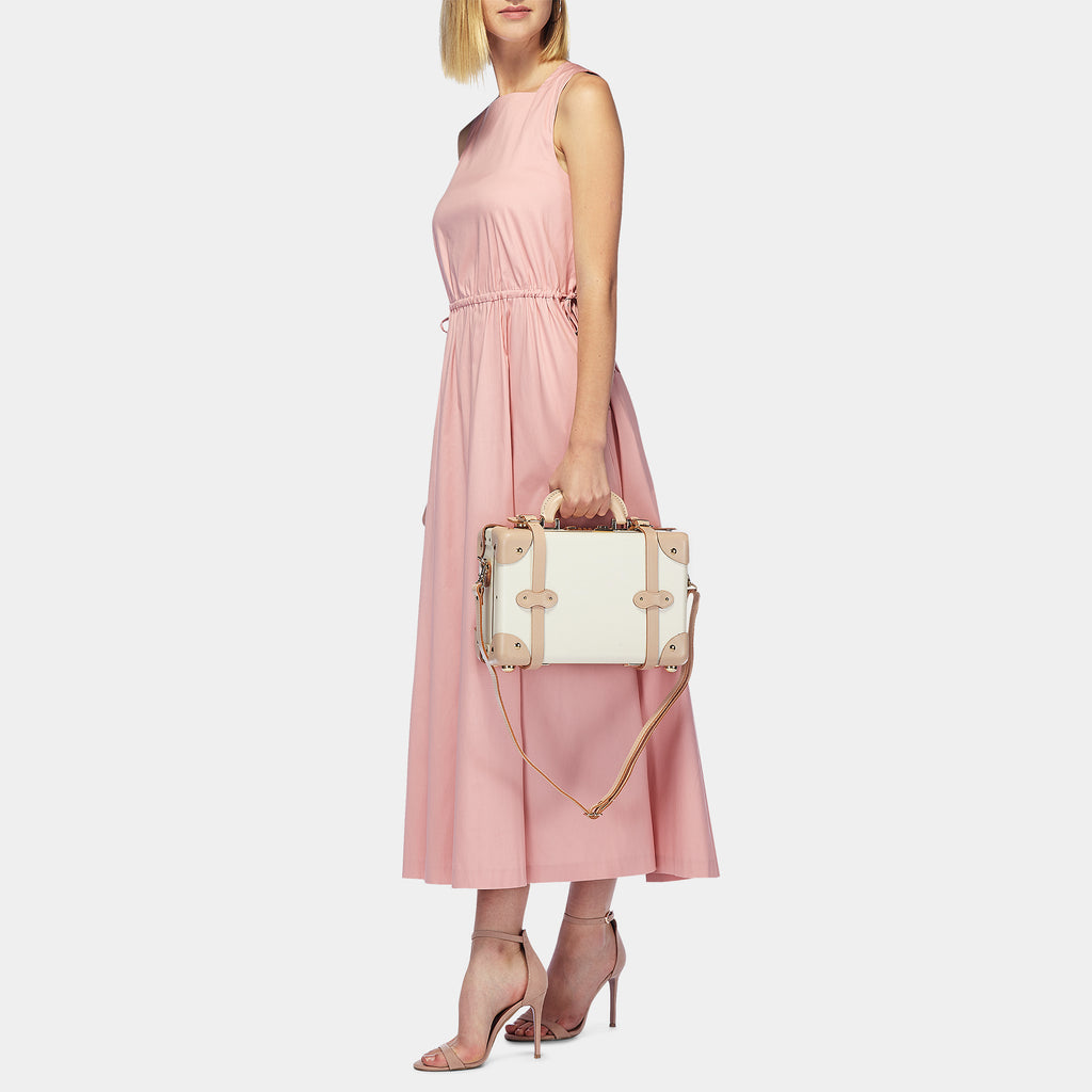 Woman in a pink dress holding a white handbag with gold accents on a light gray background