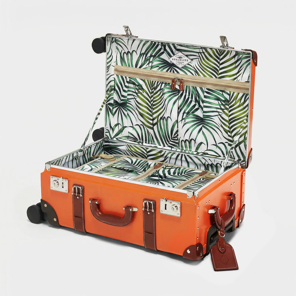Orange suitcase with tropical leaf pattern interior on a white background