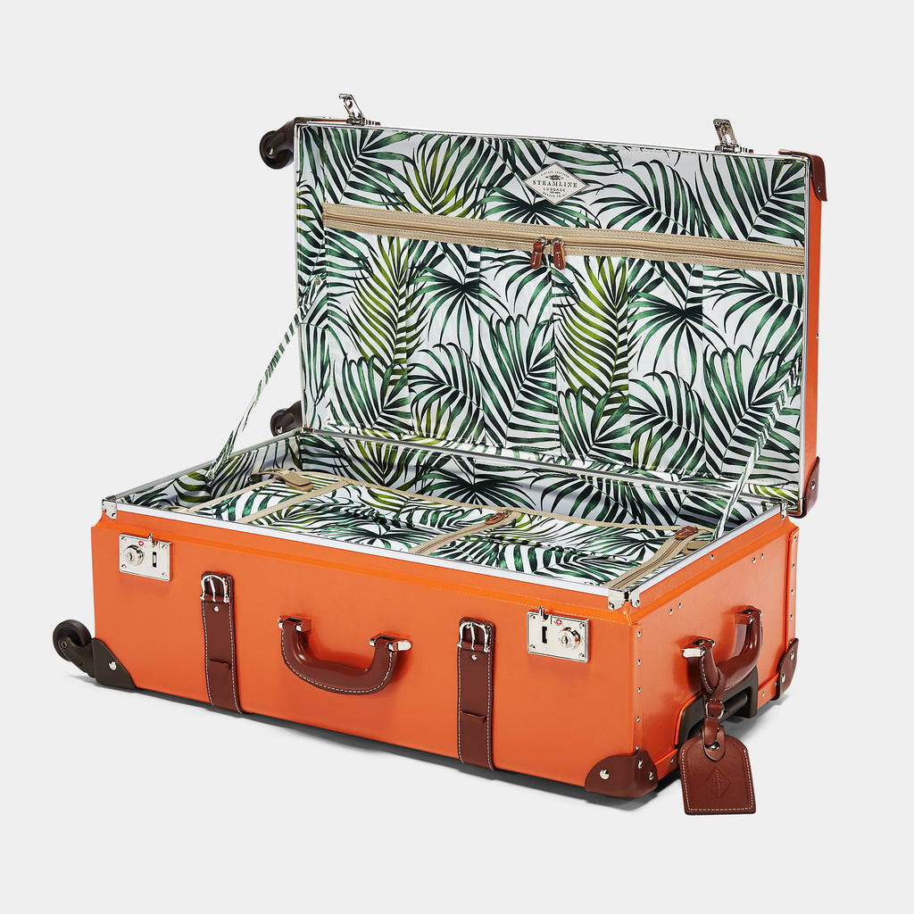 Orange suitcase with a tropical leaf pattern interior on a white background