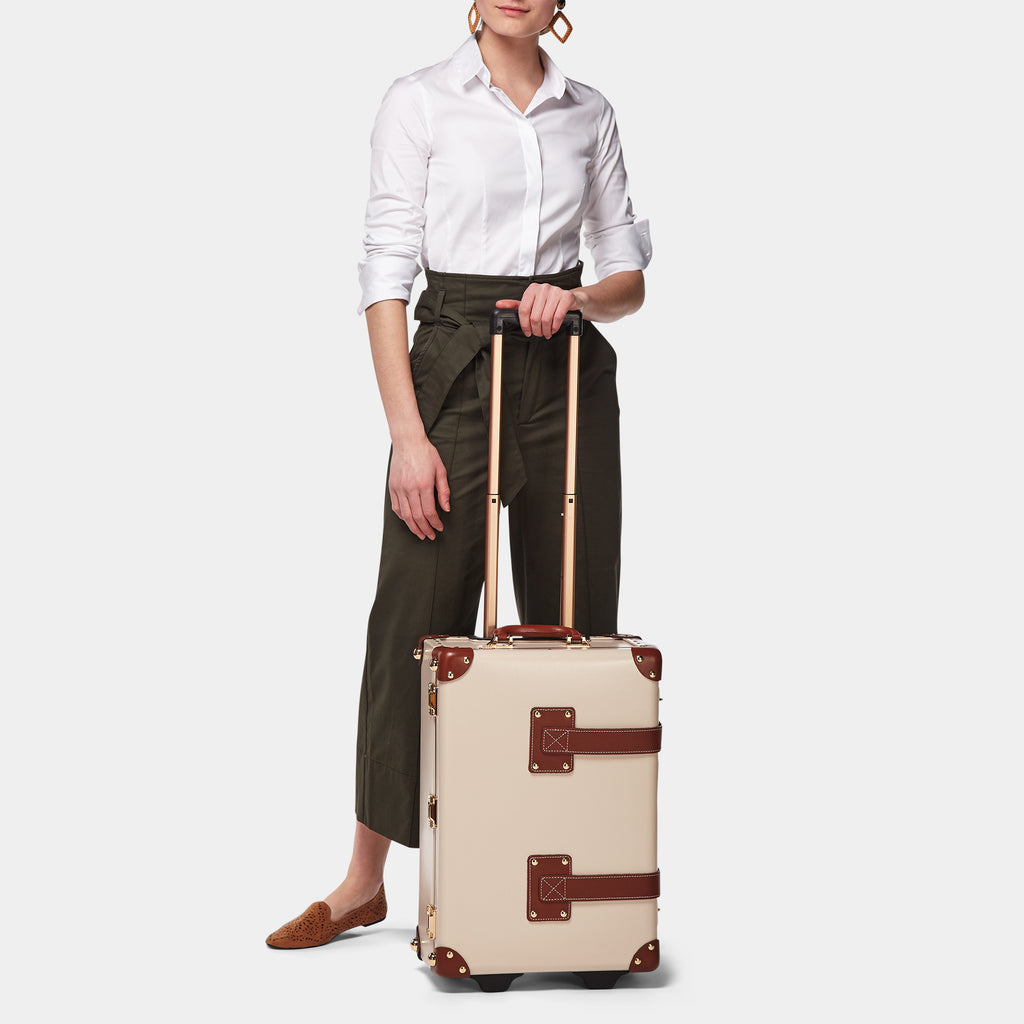 Person holding a beige suitcase with brown accents on a white background