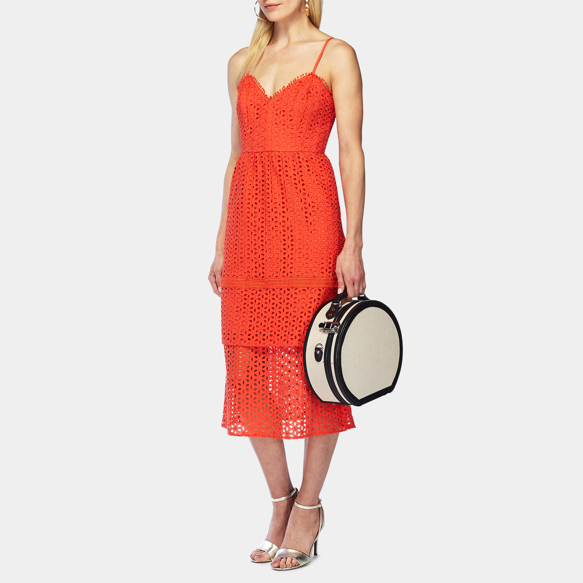 Woman wearing a red lace dress holding a black and white handbag on a white background