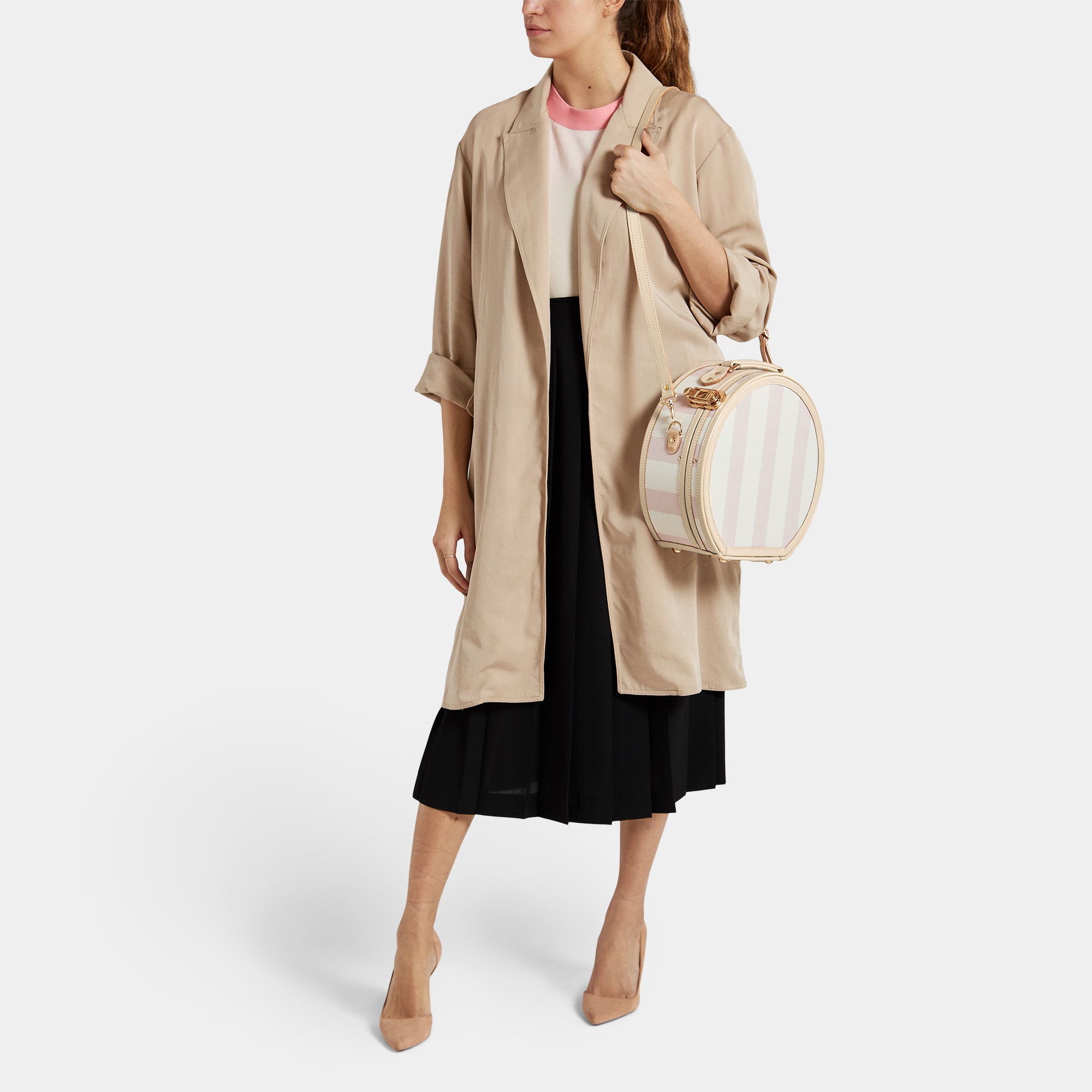 Woman holding a round, striped bag wearing a beige trench coat on a white background