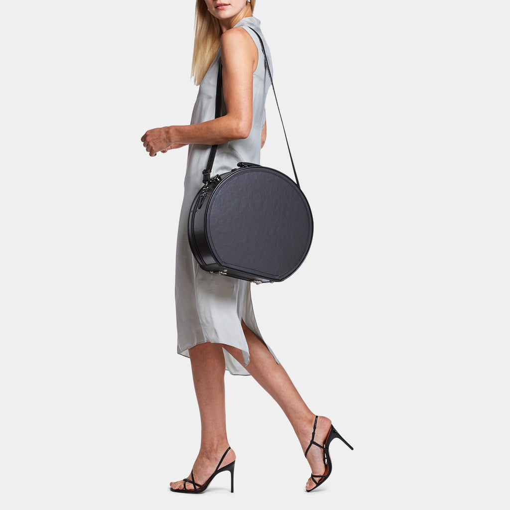 Woman holding a black round handbag against a white background