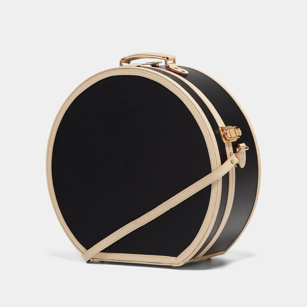 Round black hatbox suitcase with gold accents on a light gray background