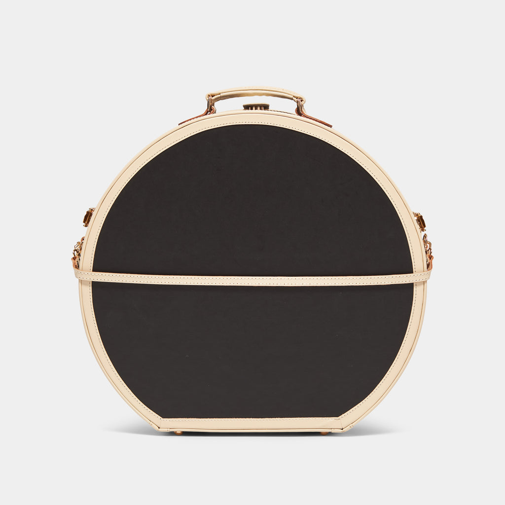 Black round hatbox with beige trim on a light gray background