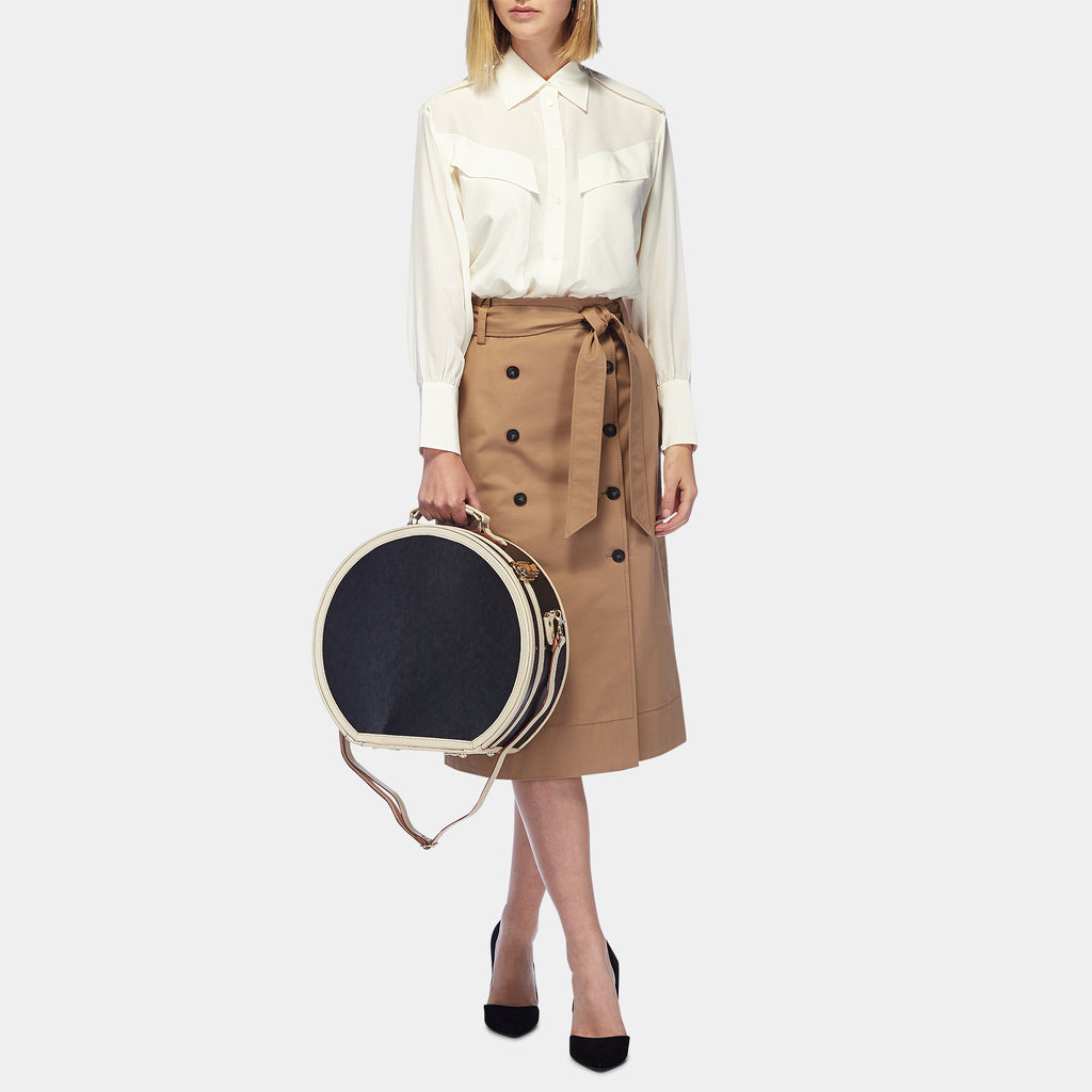 Person holding a round black and beige handbag wearing a white blouse and tan skirt.