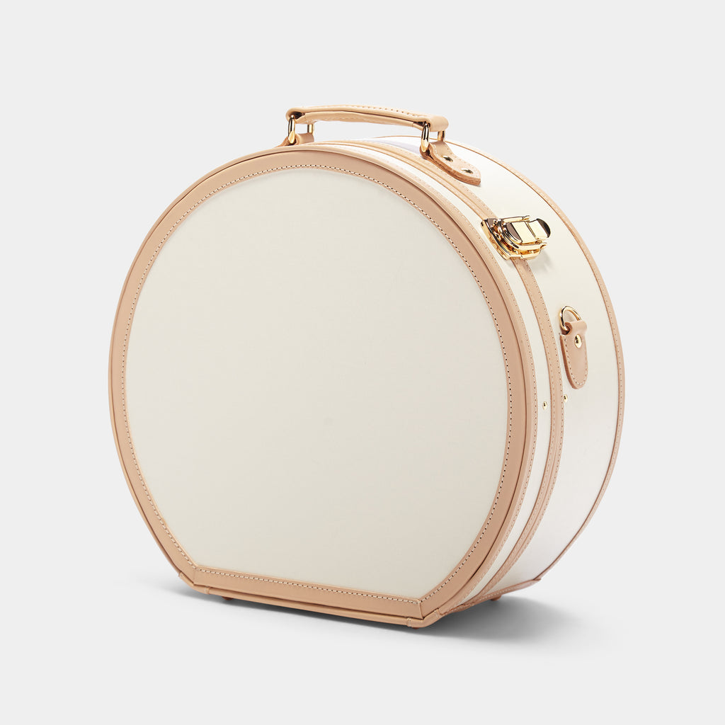 Round beige travel case with gold accents on a light gray background