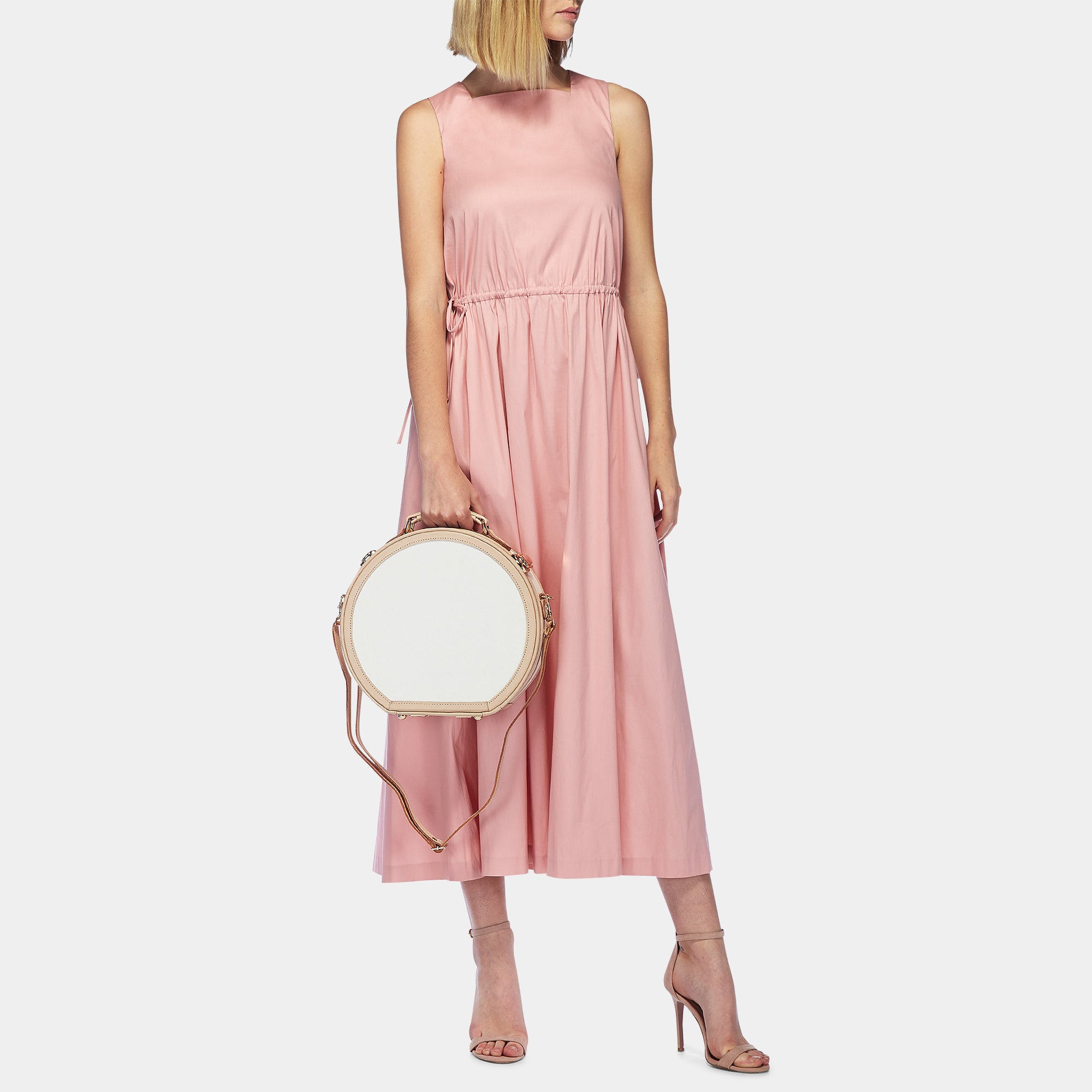 Woman wearing a pink dress holding a round handbag on a light gray background