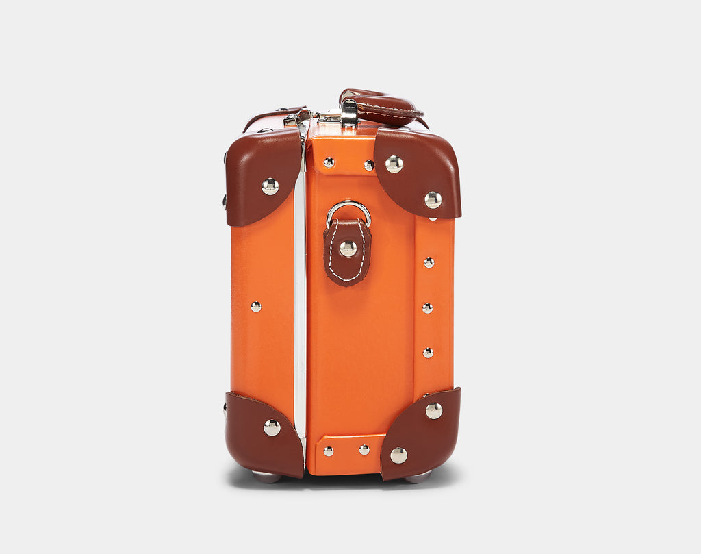 Orange suitcase with brown leather accents on a light gray background
