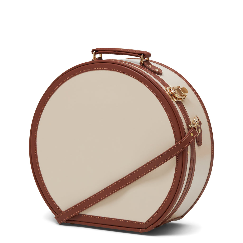 Round beige handbag with brown strap and handle on a white background