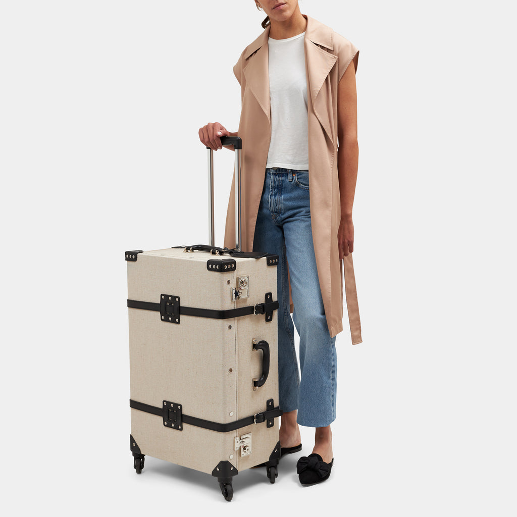 Person holding a beige suitcase with black accents on a white background