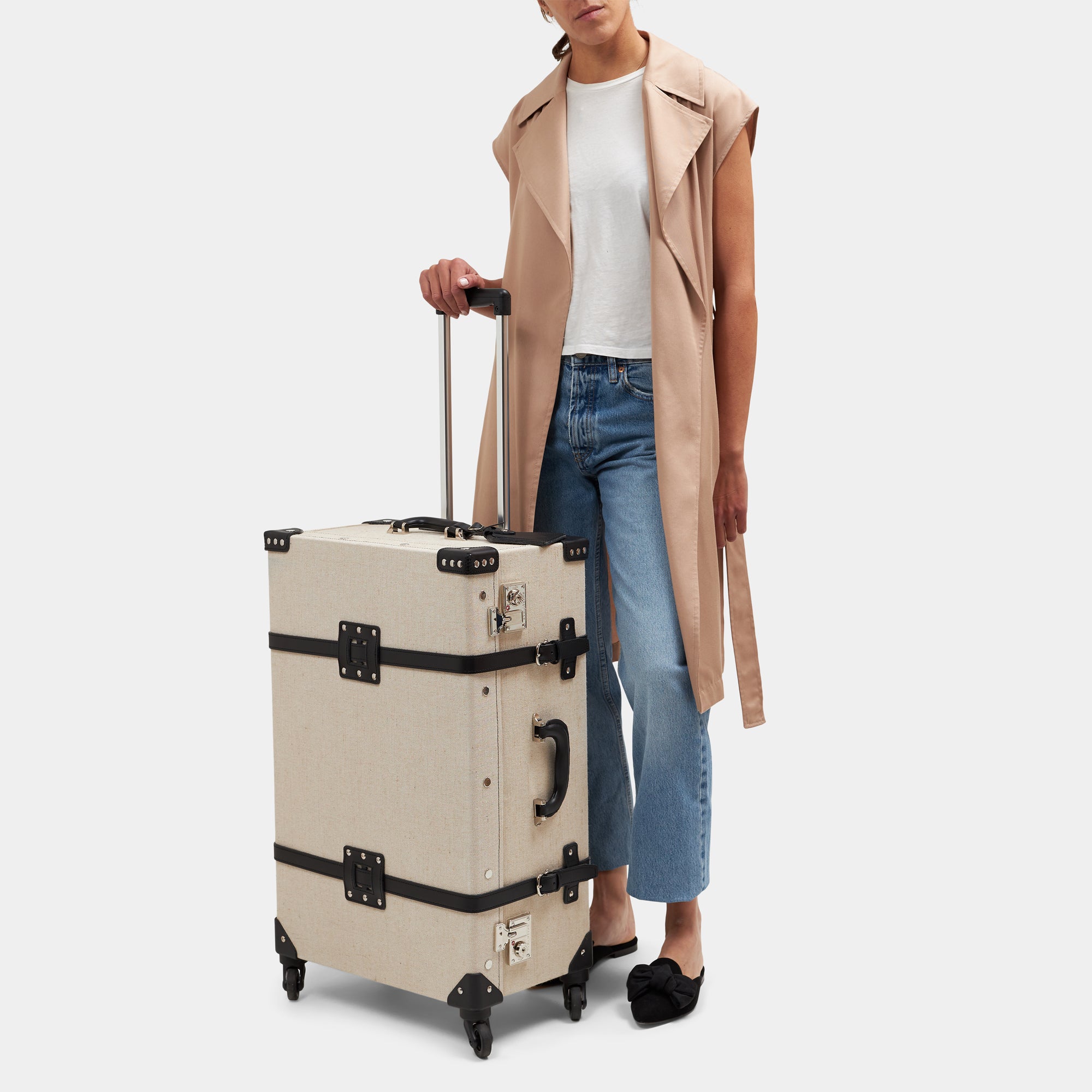 Person holding a beige suitcase with black accents on a white background