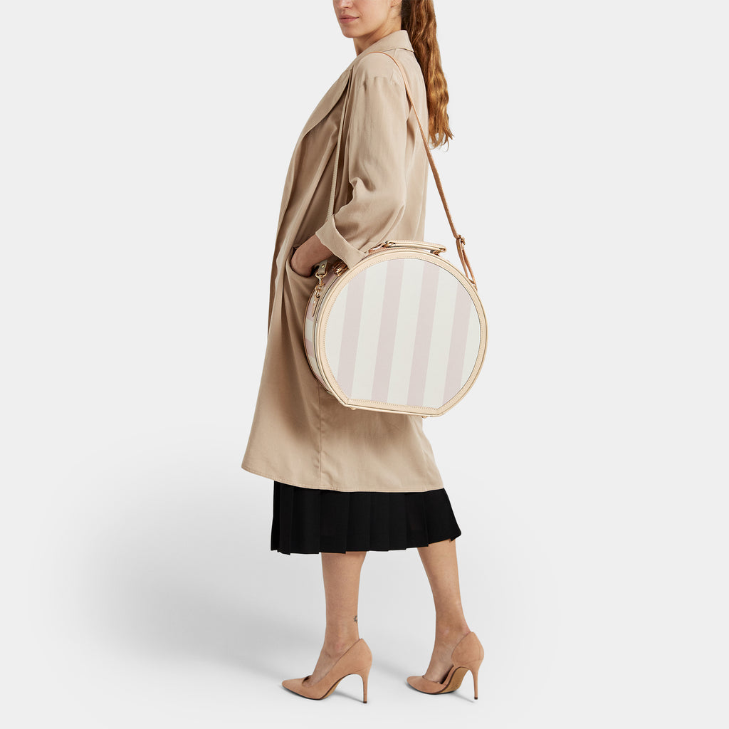 Woman holding a round, beige handbag against a white background