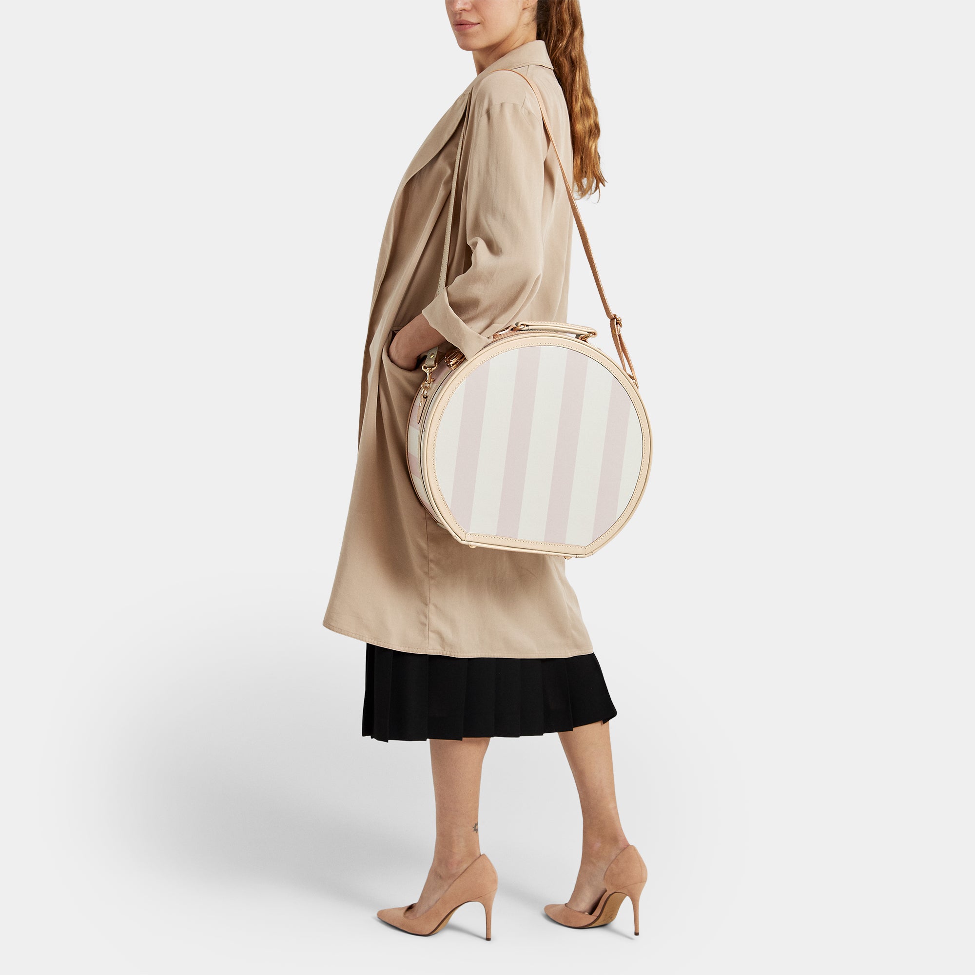 Woman holding a round, beige handbag against a white background