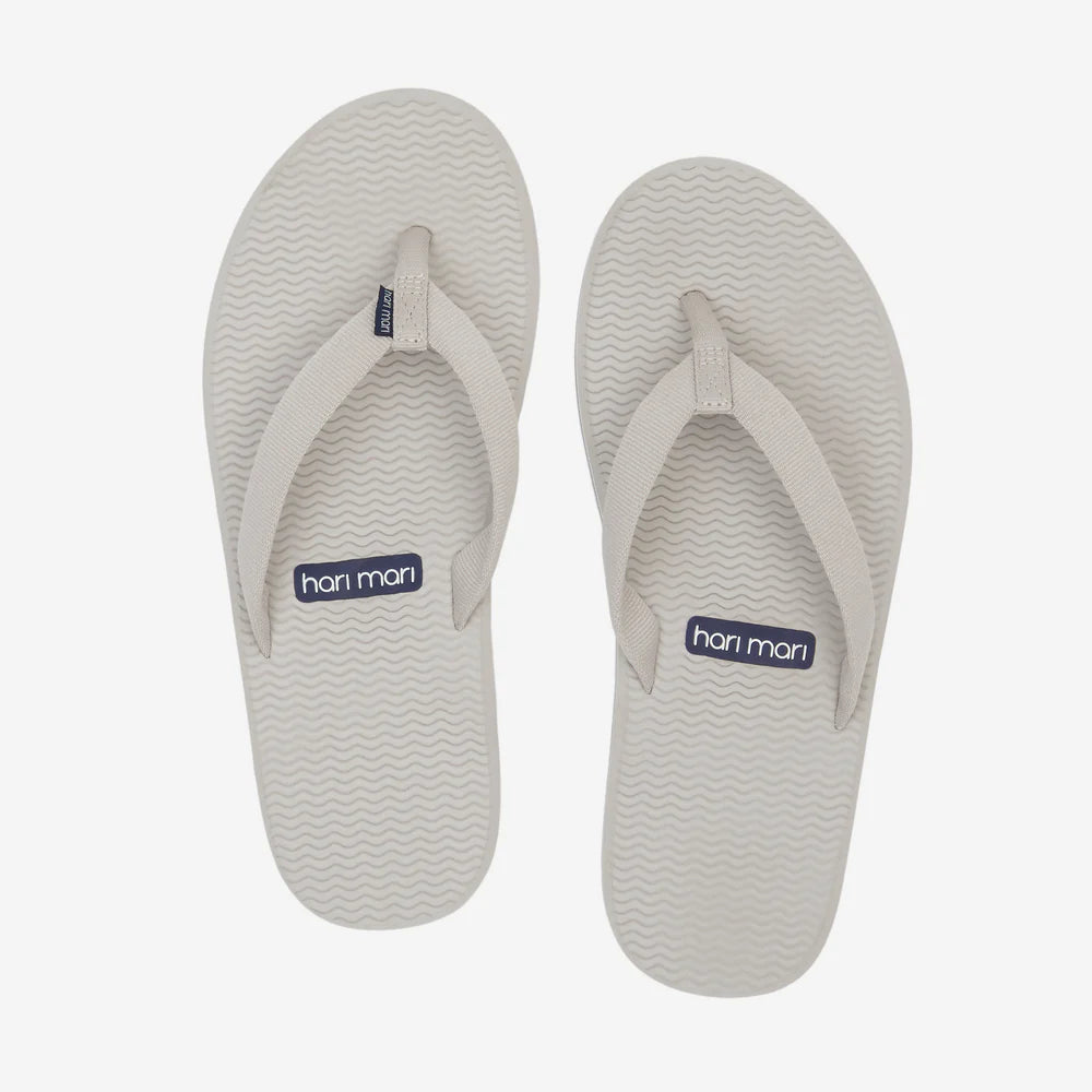 Pair of white flip-flops with 'hari mari' branding on a light gray background